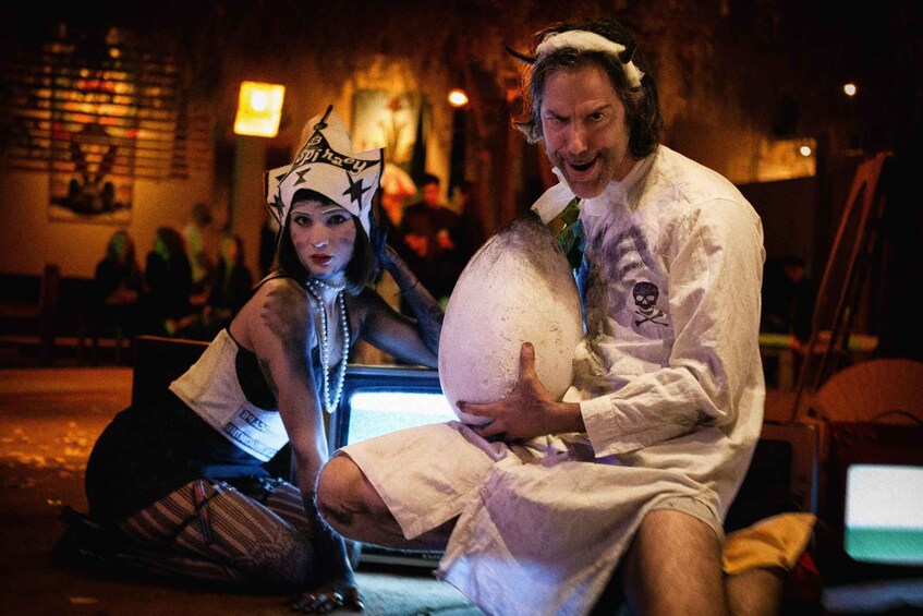 Two people in costumes, one holding a large white object, in a dimly lit indoor setting. 1