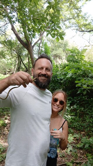 Two people standing in a forested area with trees and greenery in the background. 4