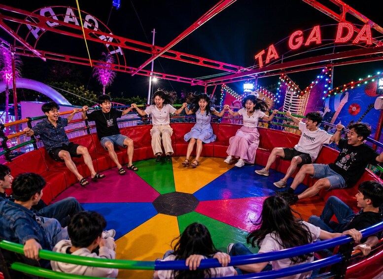 A group of people on a colorful amusement ride with a sign that reads 'TA GA DA'. 2