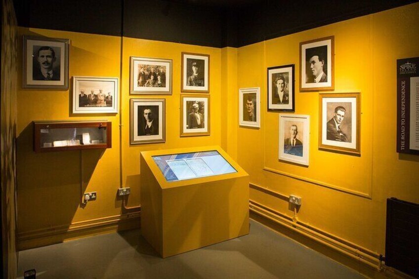 A museum exhibit with yellow walls, framed photographs, and a display case. 4