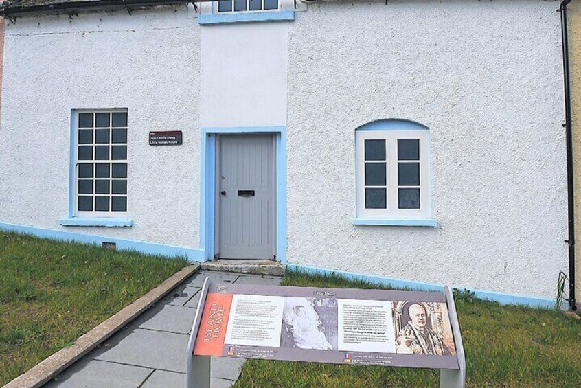 A white building with blue trim, a door, and two windows. There is a sign with text and images in front of the building. 3