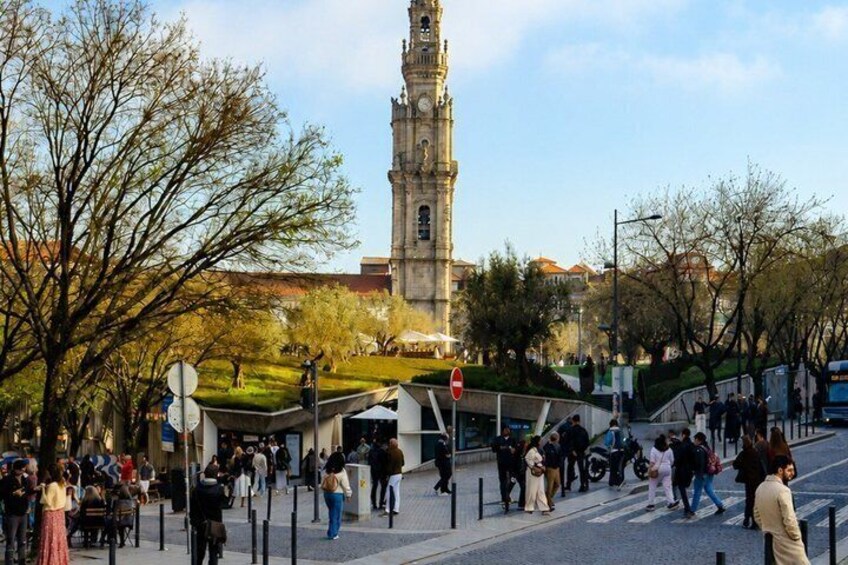 A busy urban square with a prominent clock tower, people walking, and a tram line. 4