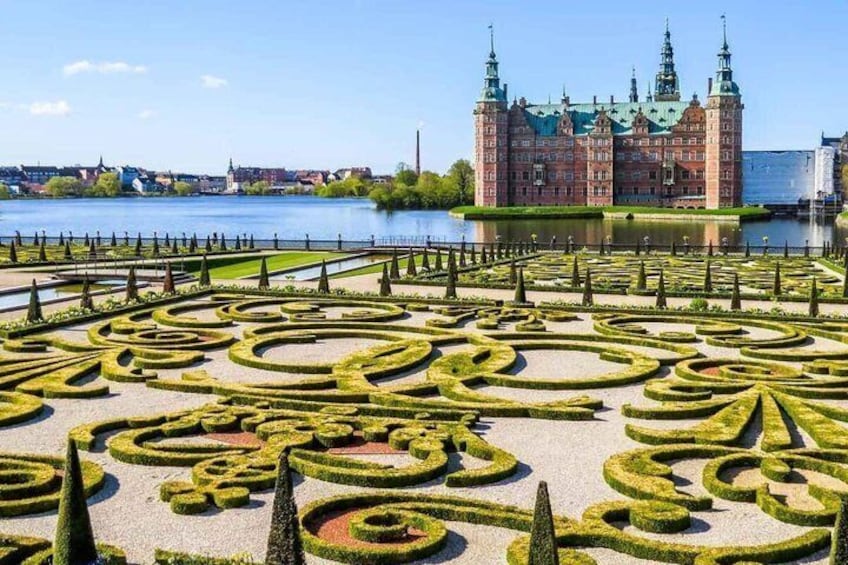 A formal garden with geometric patterns, a large building with towers, and a river in the background. 1
