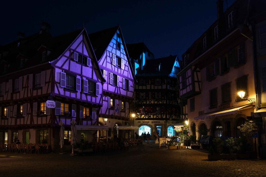 A nighttime view of a European town square with traditional half-timbered buildings and a cobblestone street. 1