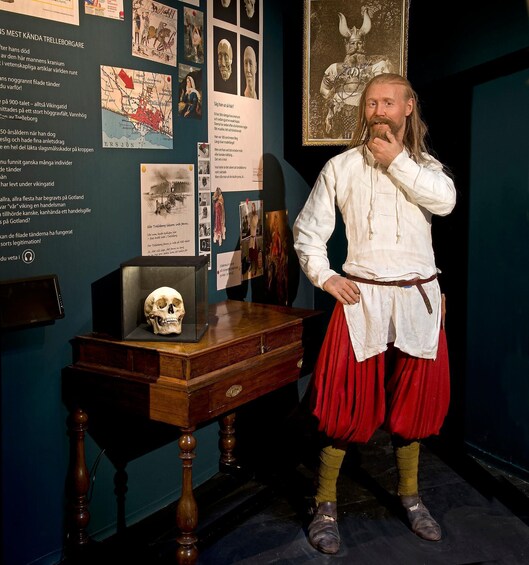 A person in historical costume standing next to a display with a skull and various informational posters. 3