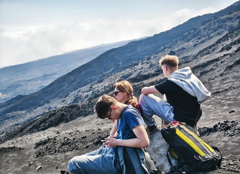 Three people sitting on a rocky outcrop with a mountainous landscape in the background. 1