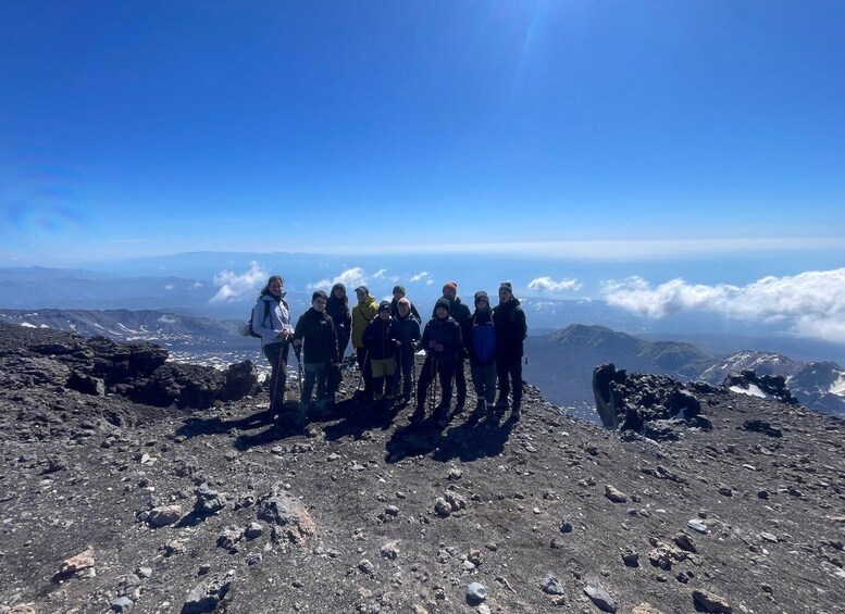A group of hikers on a rocky mountain peak with a clear sky and distant clouds. 2
