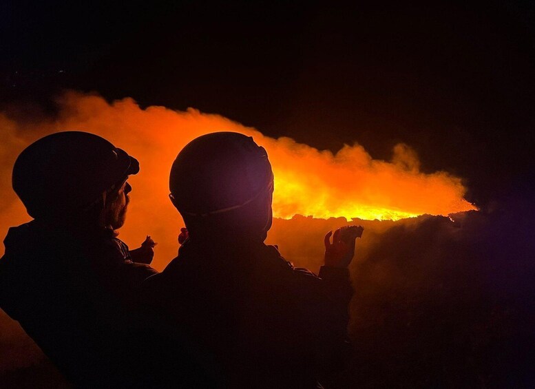Silhouettes of two people in military attire observing a volcanic eruption with lava and smoke. 1