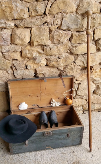 A wooden chest with a cane, a black hat, and shoes against a stone wall. 2