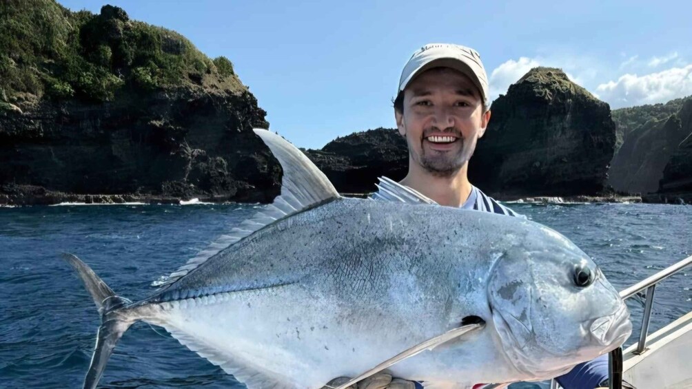 A person holding a large fish on a boat with a mountainous coastline in the background. 2