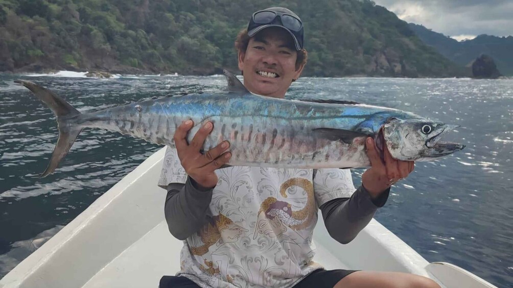 A person holding a large fish on a boat with a mountainous landscape in the background. 5