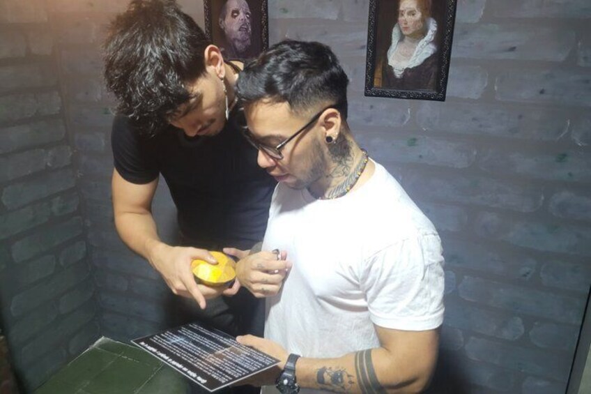 Two people examining a book and a yellow object in a room with brick walls and framed pictures. 4