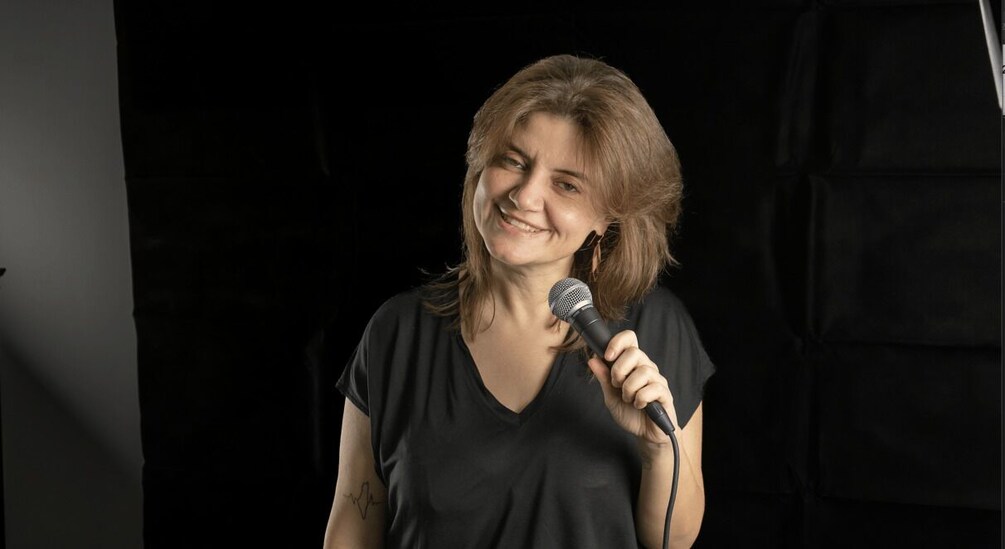 A person holding a microphone, wearing a black shirt, with a dark background. 4