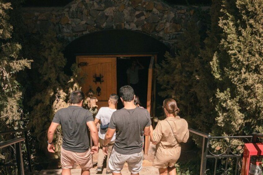 A group of people ascending stone steps towards a wooden door with a stone wall and foliage around. 1