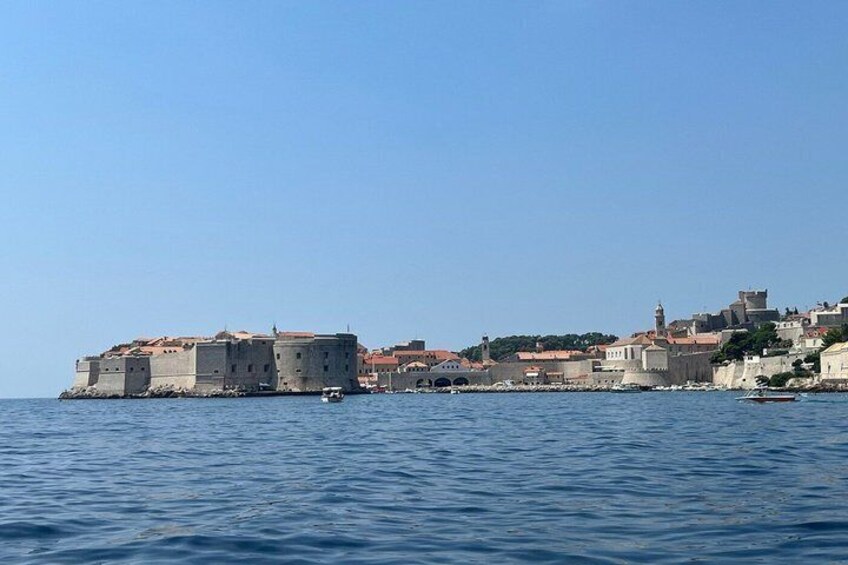 A coastal cityscape with a prominent fortress-like structure, a clear blue sky, and calm sea. 3