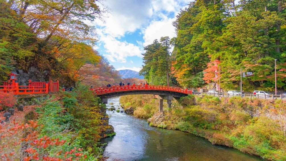 A red bridge over a river, surrounded by autumn foliage and a mountainous backdrop. 4