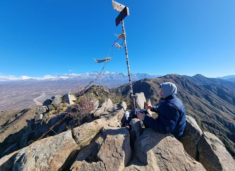 A person sitting on a rocky outcrop with a mountain view in the background. 1
