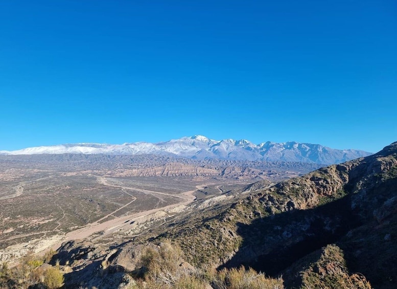 A mountainous landscape with a clear sky, a winding road, and snow-capped peaks in the distance. 2