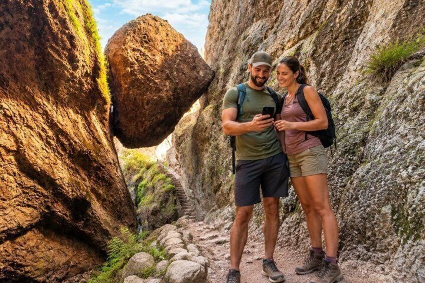 Two people hiking on a rocky trail with large boulders and sparse vegetation. 3