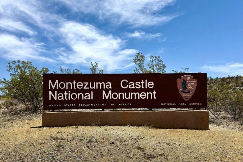 A sign for the Montezuma Castle National Monument with a clear sky and desert landscape. 1