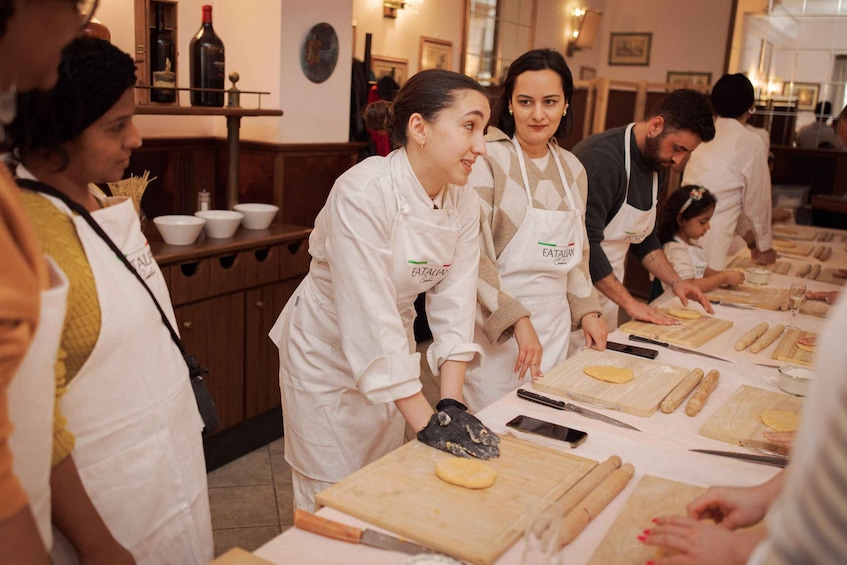 A group of people in a kitchen, wearing aprons, preparing food. 4