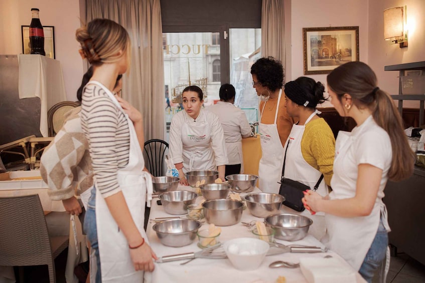A group of people in a kitchen, wearing aprons, with bowls and cooking utensils on the table. 3