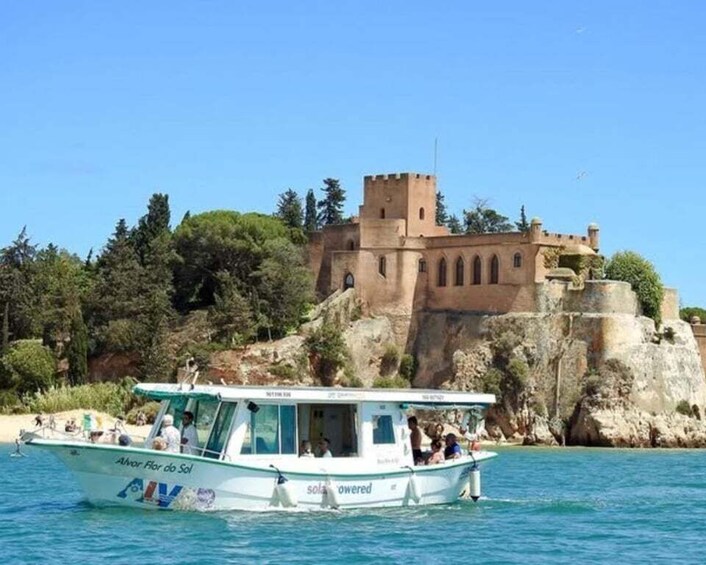 A boat named 'Alvor Flor do Sol' on calm waters with a historic castle in the background. 1