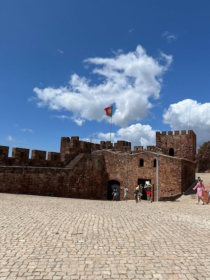 A historic stone fortress with a flag, cobblestone courtyard, and tourists. 5