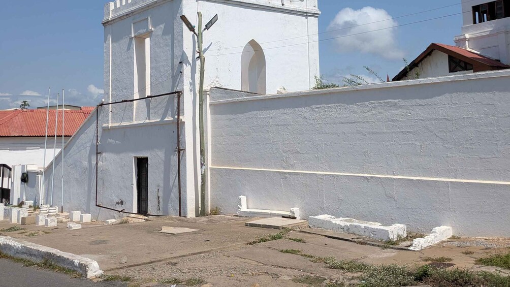 A white church with a bell tower, a paved courtyard, and a red-roofed building in the background. 5