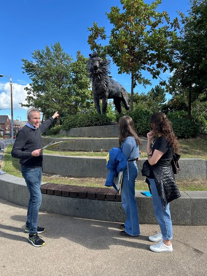 A man pointing at a lion statue surrounded by trees. 2