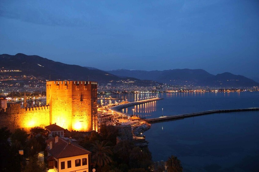 A coastal cityscape at dusk with a prominent tower and a long pier extending into the water. 1