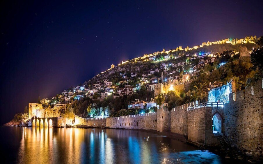 A historic fortified city at night with illuminated buildings and a prominent castle on a hill overlooking a calm body of water. 4