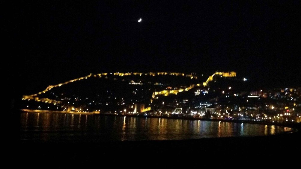 A cityscape at night with illuminated buildings and a crescent moon in the sky. 5