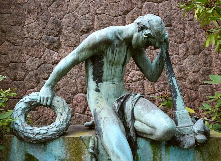 A bronze statue of a man with a rope, set against a stone wall. 3