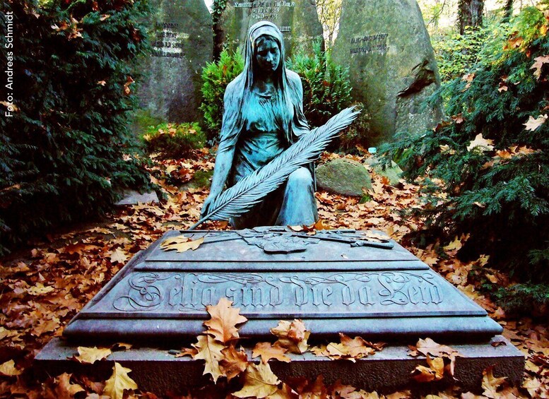 A statue of a woman holding a feather, surrounded by autumn leaves, with a stone inscription in front. 5