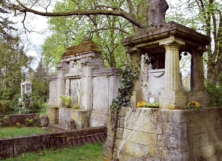A cemetery with stone monuments, some covered in moss, and a small structure with a roof. 2