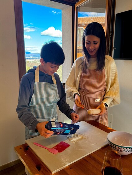 Two people in a kitchen preparing food, with a window showing a view of a house and mountains. 4