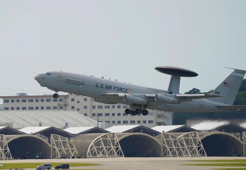 A U.S. Air Force aircraft landing at an airport with hangars in the background. 3