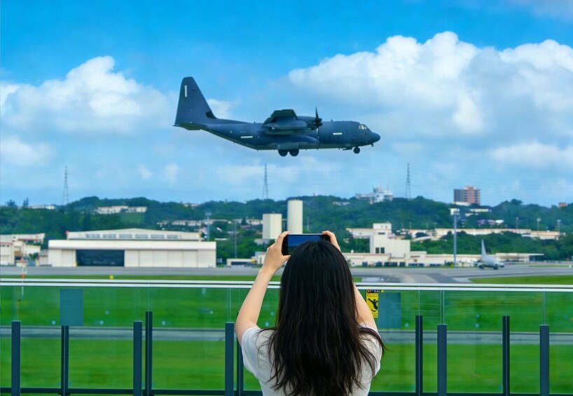 A person taking a photo of a military aircraft flying over a runway. 2