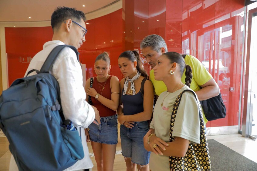 A group of people standing in a hallway with red walls and a glass door. 2