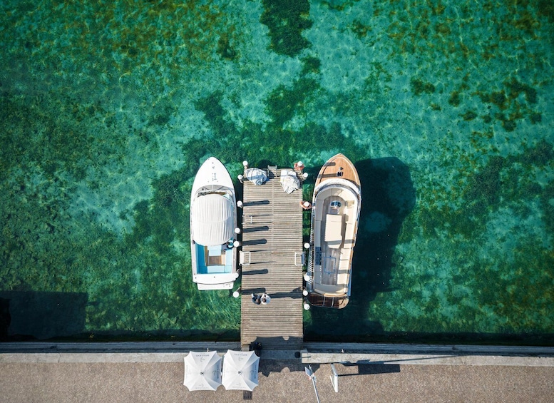 Two boats docked at a pier with clear water and green seaweed. 3