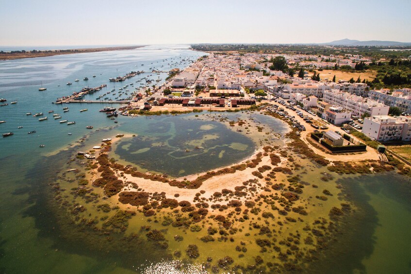 An aerial view of a coastal town with a marina, buildings, and a distinctive circular water feature surrounded by vegetation. 1