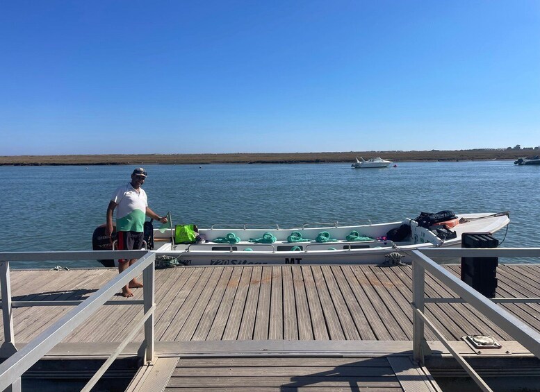 A man on a wooden dock with a boat, a calm sea, and a distant shoreline. 4