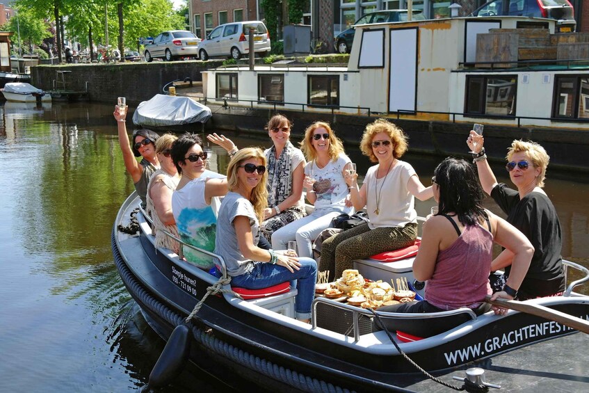 A group of people on a boat with food, a canal, and buildings in the background. 3