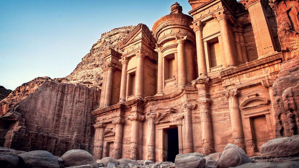 A sandstone structure with columns and a large rock formation in the background. 5