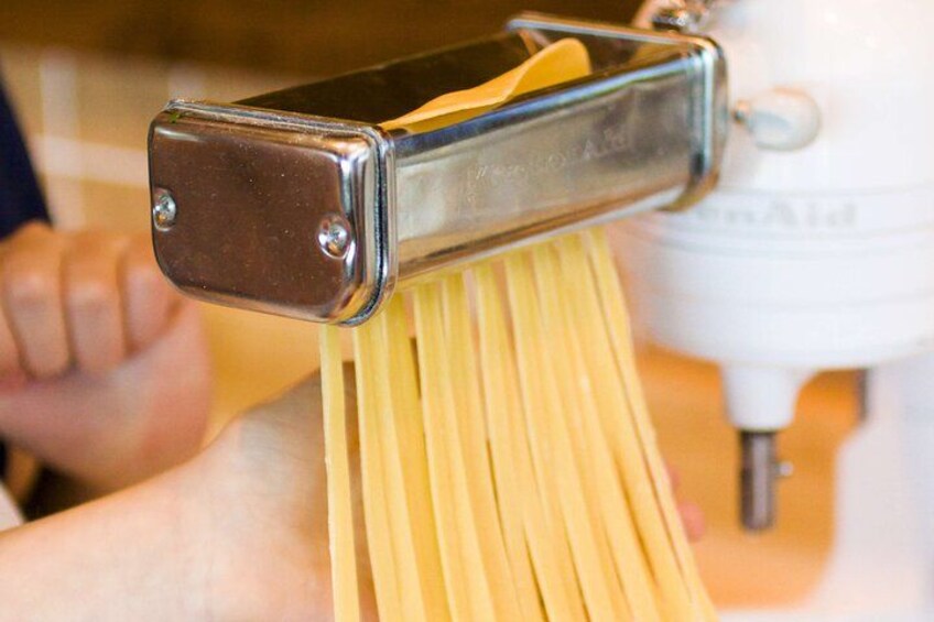 A person using a pasta machine to cut spaghetti. 2