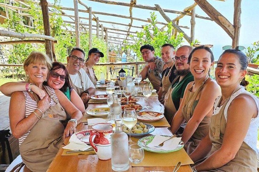 A group of people dining at an outdoor wooden table with food and drinks. 4