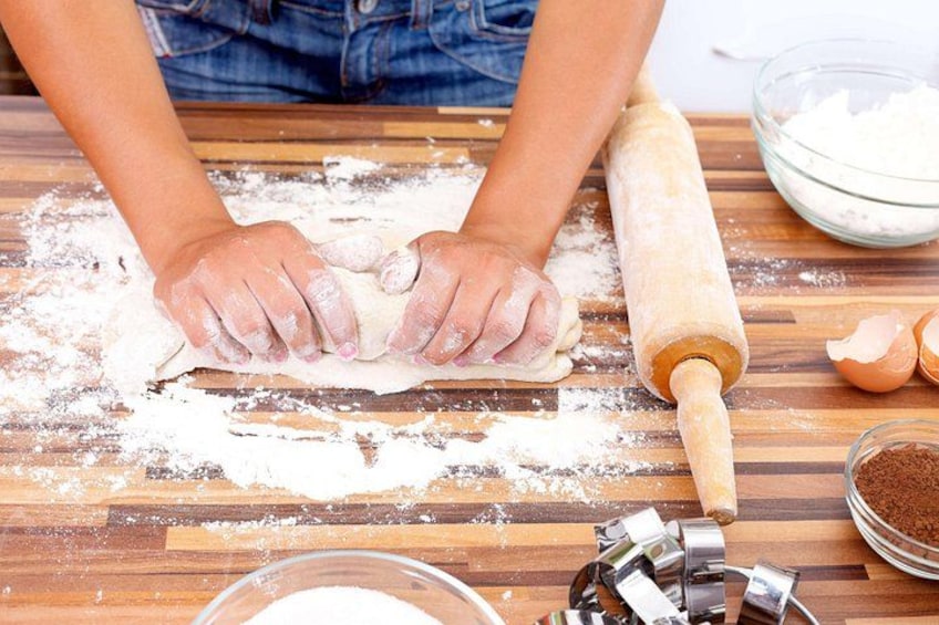 Una persona extiende masa sobre una superficie de madera, con harina esparcida alrededor, un rodillo y utensilios de repostería. 4