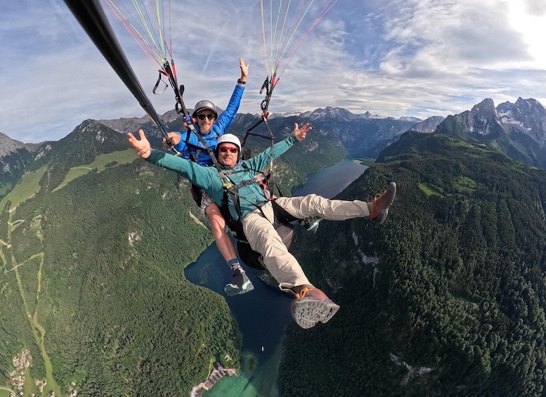 Two people paragliding over a mountainous landscape with a lake below. 1