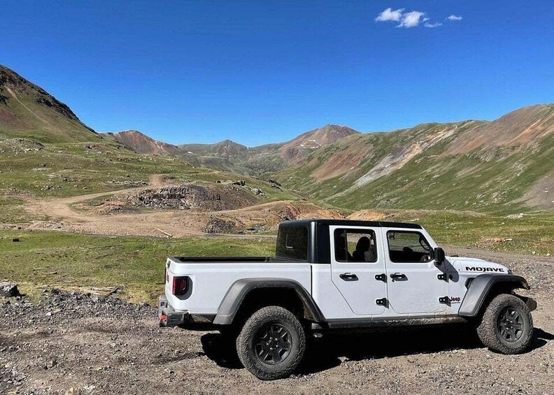 A white off-road vehicle parked on a gravel path in a mountainous area. 1